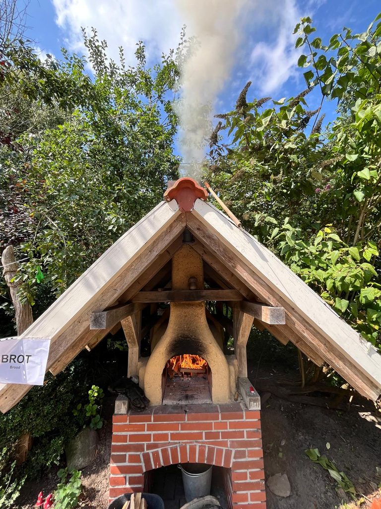 Gemauerter Holzbackofen unter einem Schutzdach im Garten